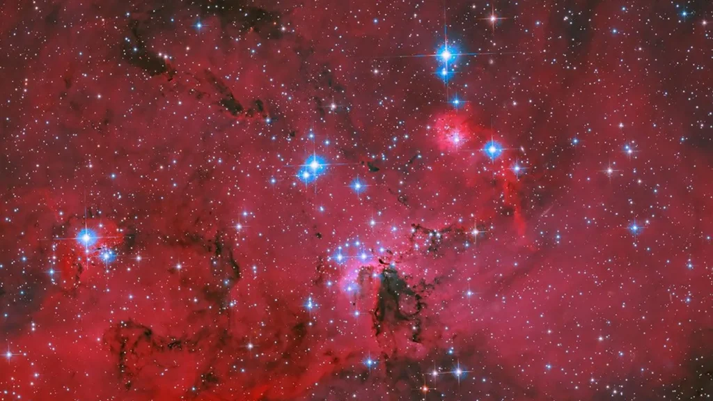 NASA’s Hubble captures a crimson stellar nursery sparkling with blue and white stars